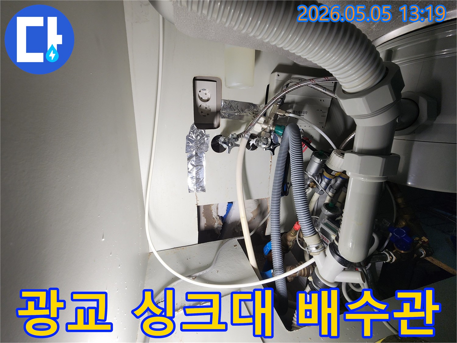 이 이미지는-광교마을-아파트의-싱크대-배수관-누수-현장을-보여주며-벽면을-개방하여-드러난-손상된-배수관과-주변-시설을-촬영한-것입니다