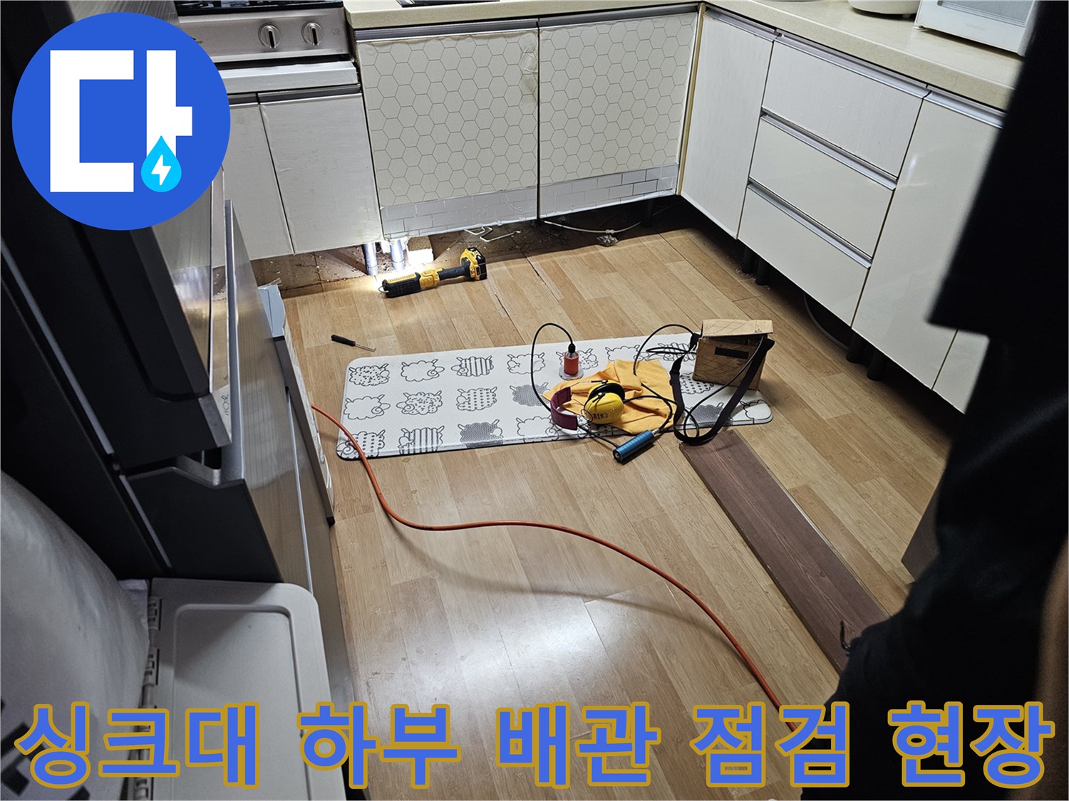 싱크대 아래쪽 노출된 공간과 바닥에 놓인 작업용 장비들