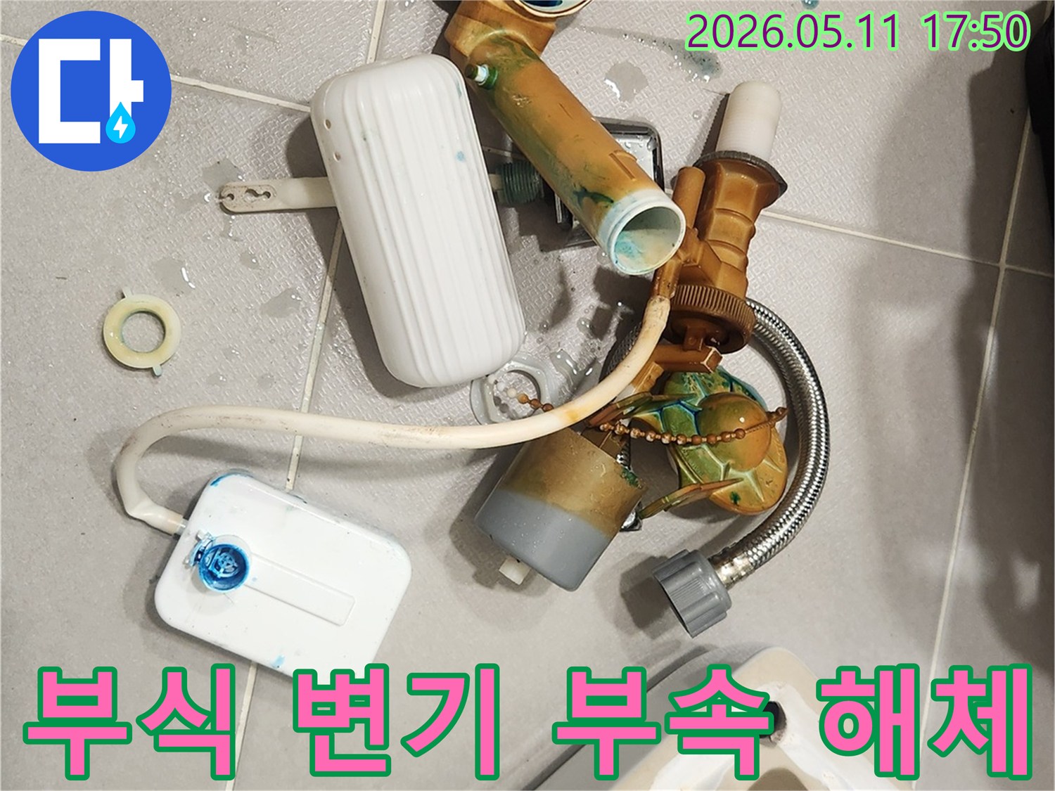 안방 변기에서 발생한 누수 문제로 인해-부식된 변기 부속들이 해체되어 바닥에 놓여 있습니다-새 부품으로 교체하여 문제를 해결할 준비가 완료되었습니다