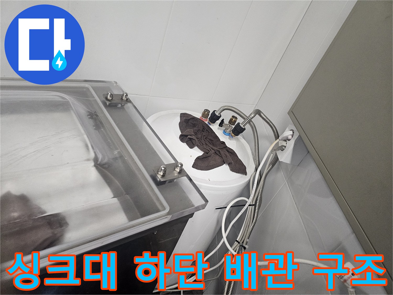 싱크대 아래쪽의 복잡한 수도 밸브와 호스 연결 부위 모습