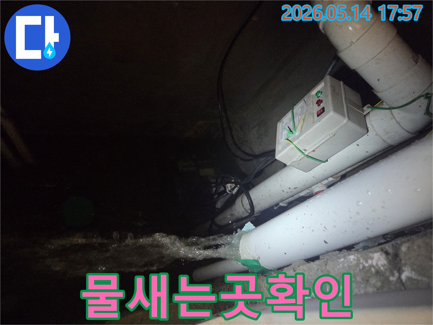 어두운 지하 공간에서-파이프에서 물이 솟구쳐 나오는-심각한 누수 현장을 보여주는 사진입니다-주변에는 전기 제어 장치와 다른 배관들이 보입니다.