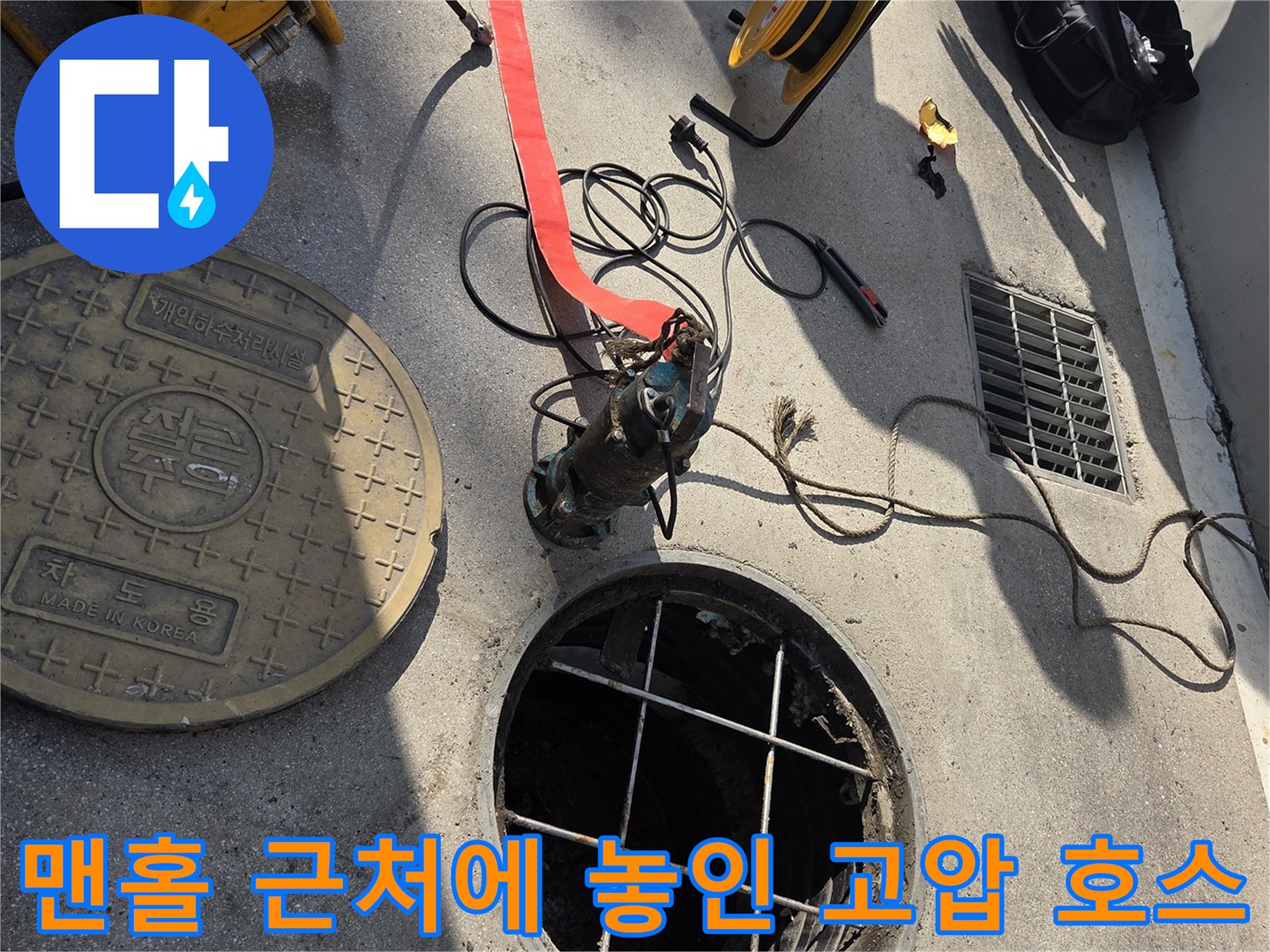 작업을 위해 맨홀 옆에 연결된 검은색 고압 호스 모습입니다.