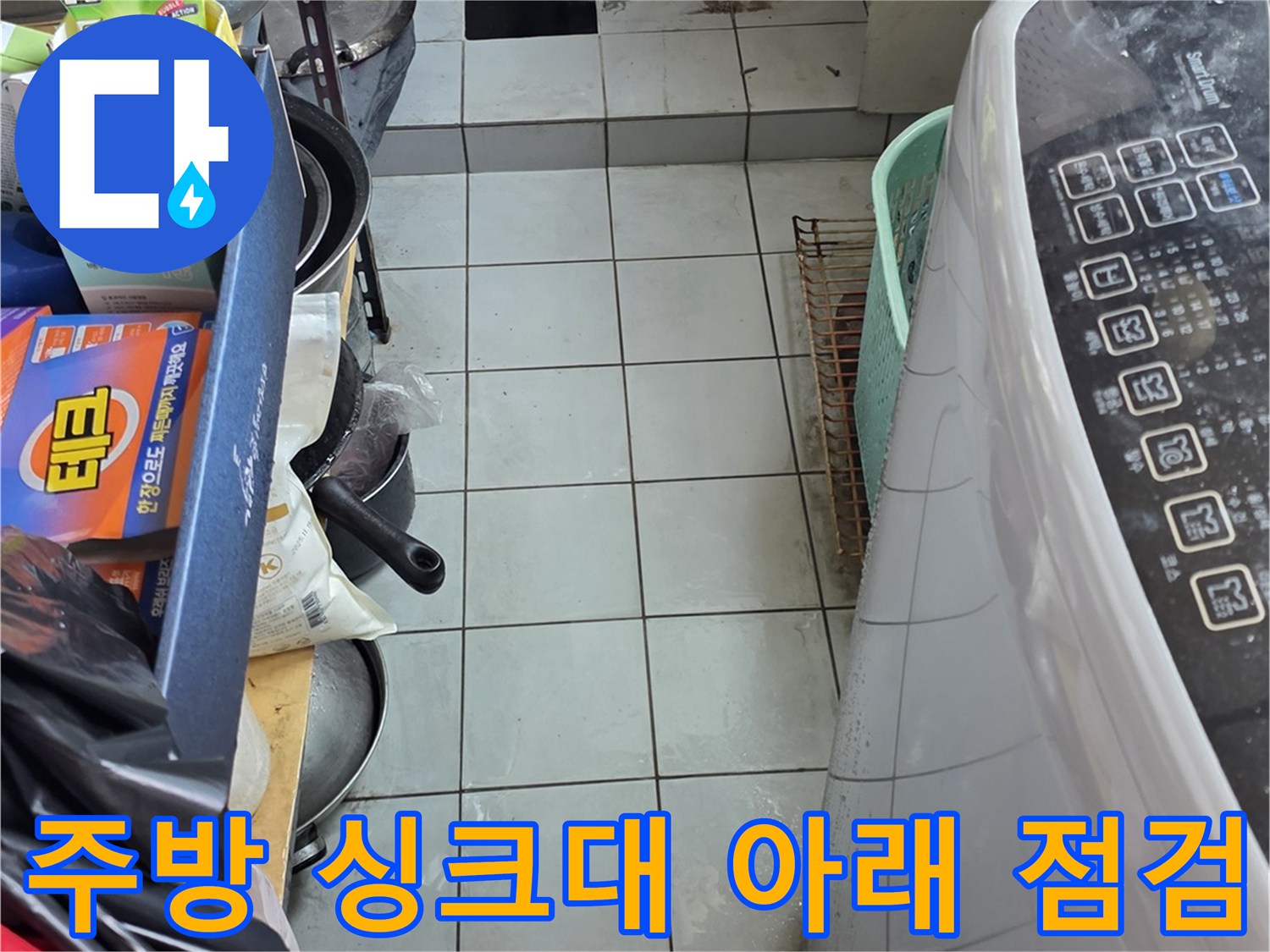 싱크대 밑 공간에 있는 배관과 주변 집기들을 촬영한 사진입니다.