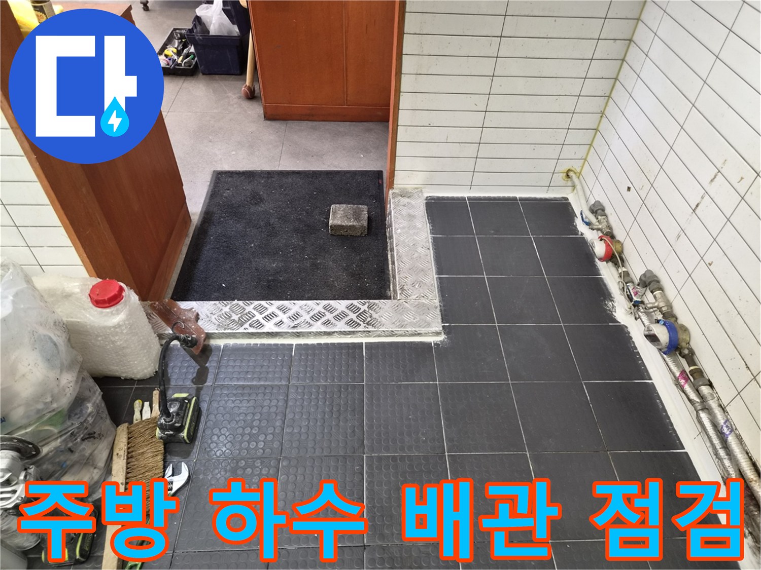 어두운 회색 타일 바닥과 벽면의 노출된 수도 배관을 촬영한 사진입니다.