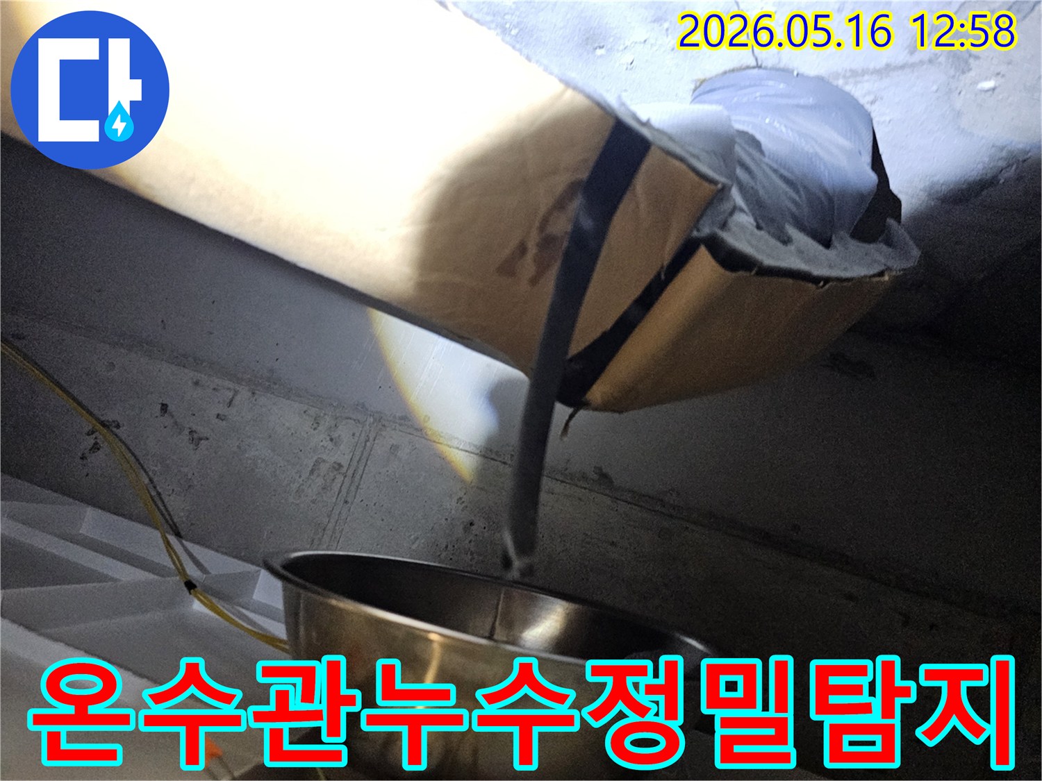 천장 속 어두운 공간에서-온수관 누수로 인해-젖은 보온재를-조명으로 비춰-확인하는 모습입니다.