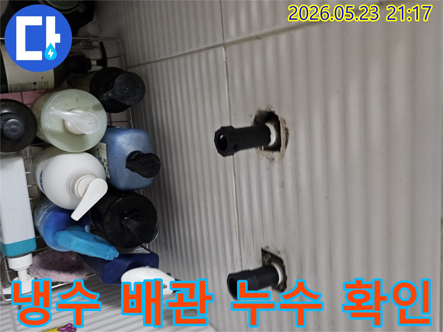 타일 벽면에서 노출된 두 개의 수도 배관 연결 부위를-냉수 배관 누수 여부를 확인하기 위해-꼼꼼하게 점검하는 모습입니다.