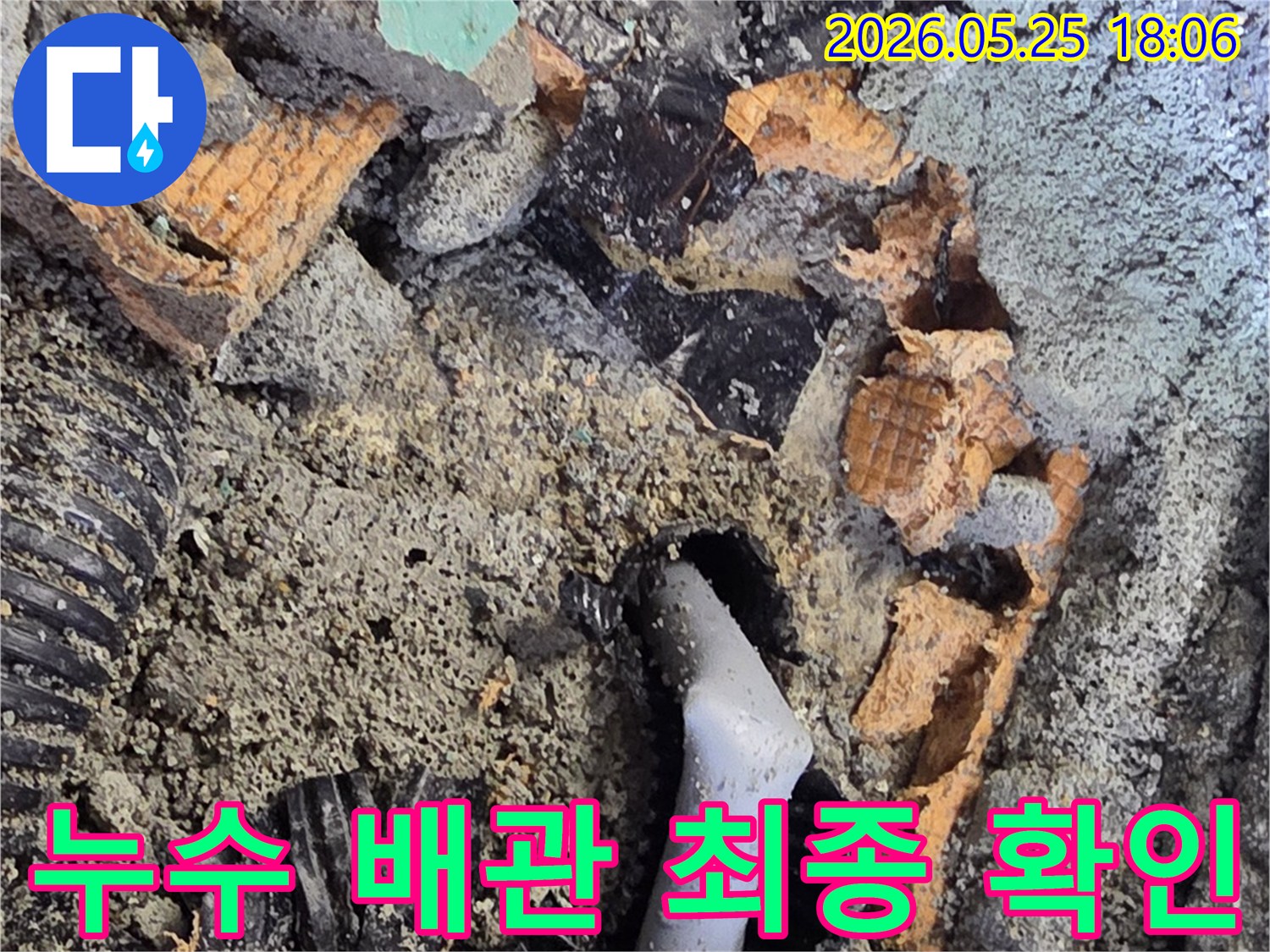 파쇄된 바닥 아래에서 드러난 젖은 배관과 주변의 흙-콘크리트 조각들은-누수 수리를 위한 배관 교체 작업을 보여줍니다.