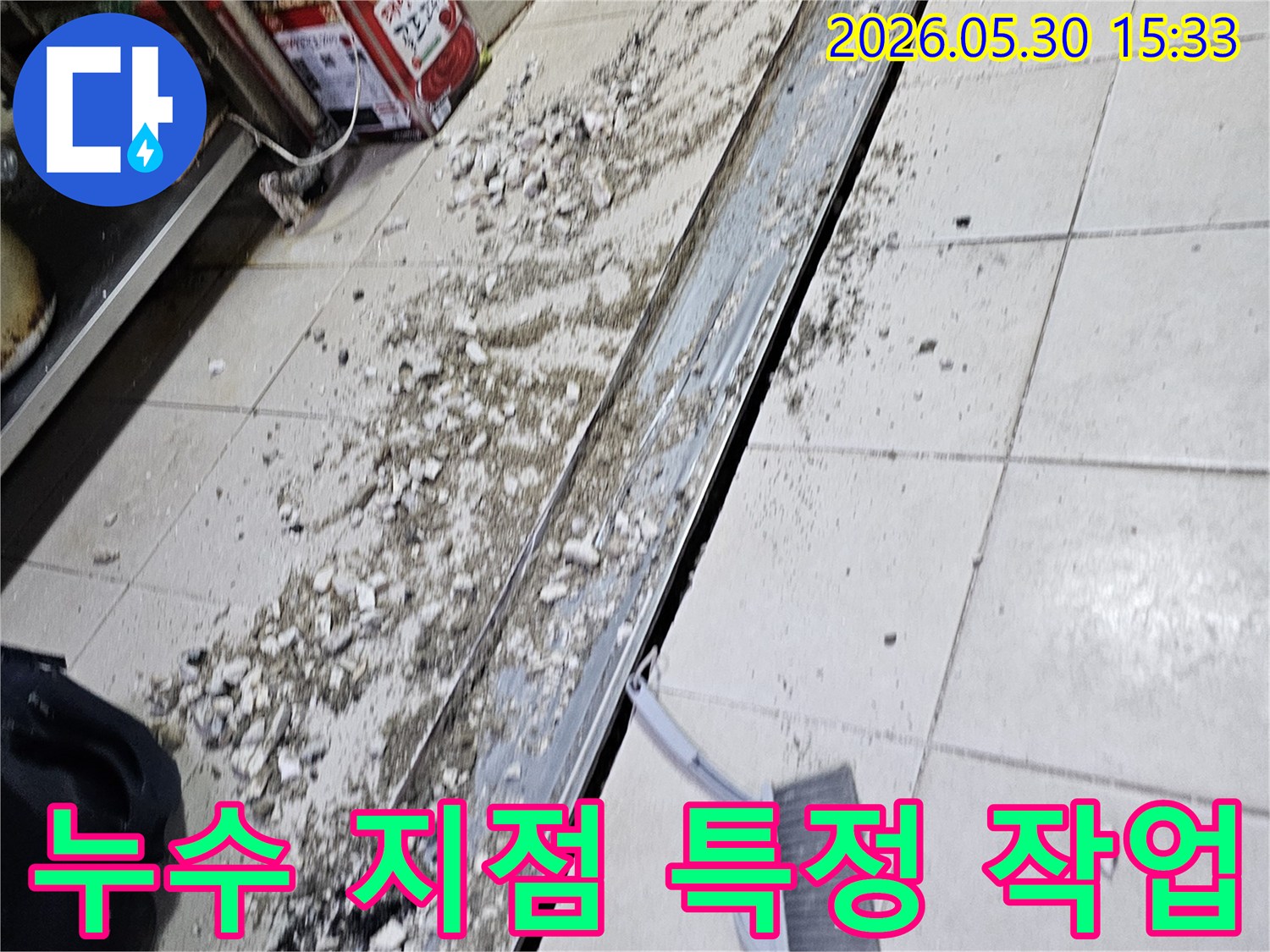 누수 공사 현장에서-바닥 타일 파쇄 후-발생한 잔해물과-청소 도구가-함께 보이는-작업 진행 모습입니다.