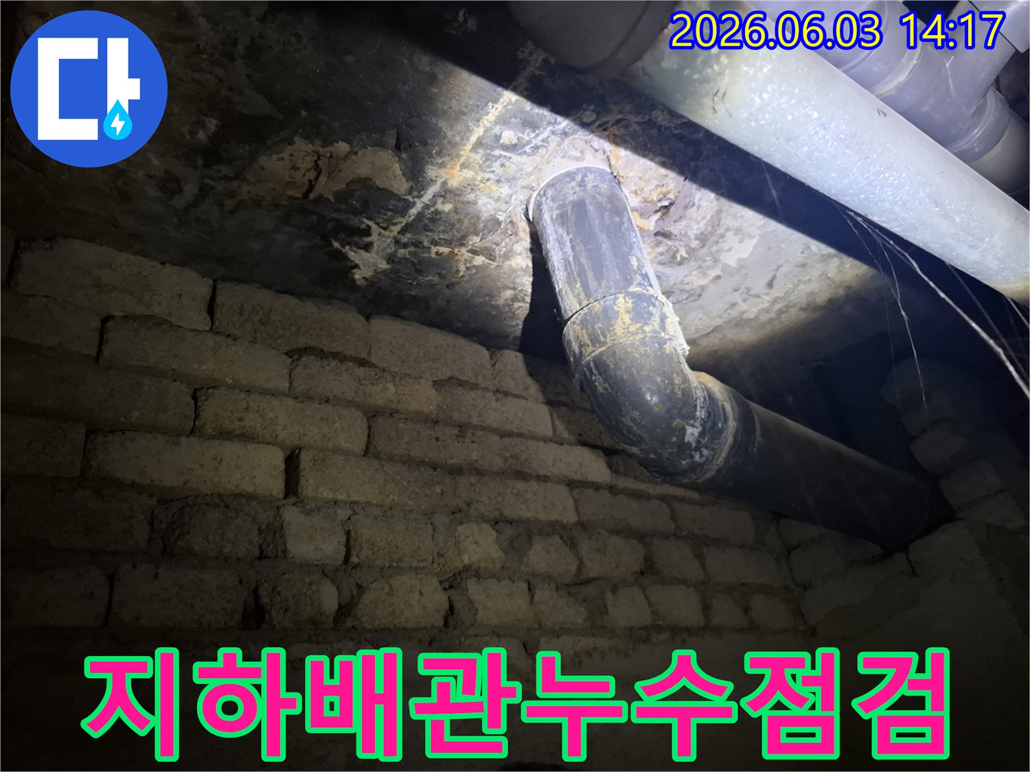어두운 지하 공간에서-낡은 배관과-벽돌 벽에 나타난-누수 흔적을-조명으로 비춰-면밀히 조사하는 모습