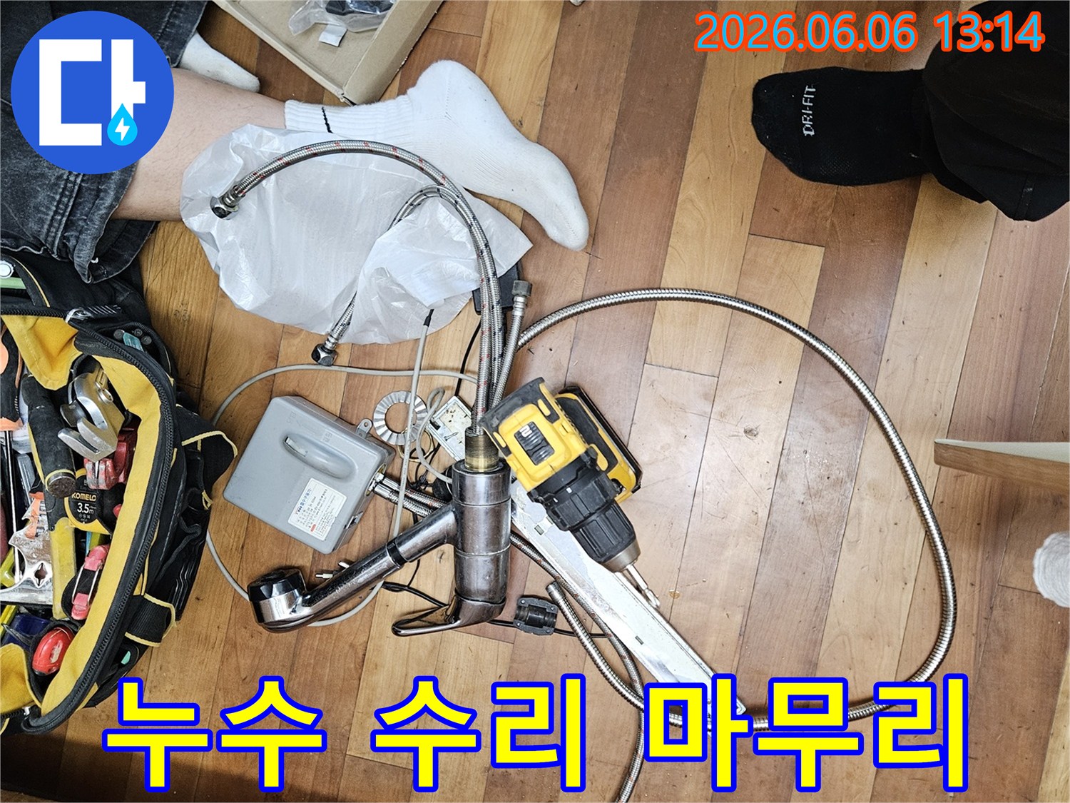 누수 공사를 위해 준비된 다양한 배관 부품과-전문가용 전동 드릴-그리고 공구 가방이 바닥에 놓여 있는 모습입니다.