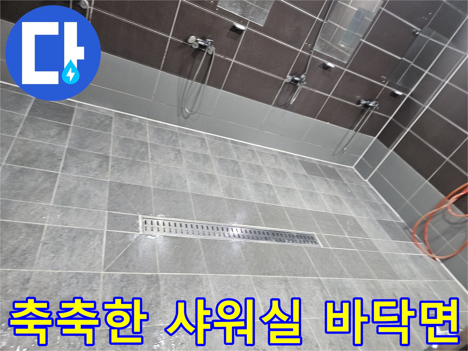 물기가 가득한 헬스장 샤워실-타일 바닥과 배수 트렌치의 상태를 나타냅니다.