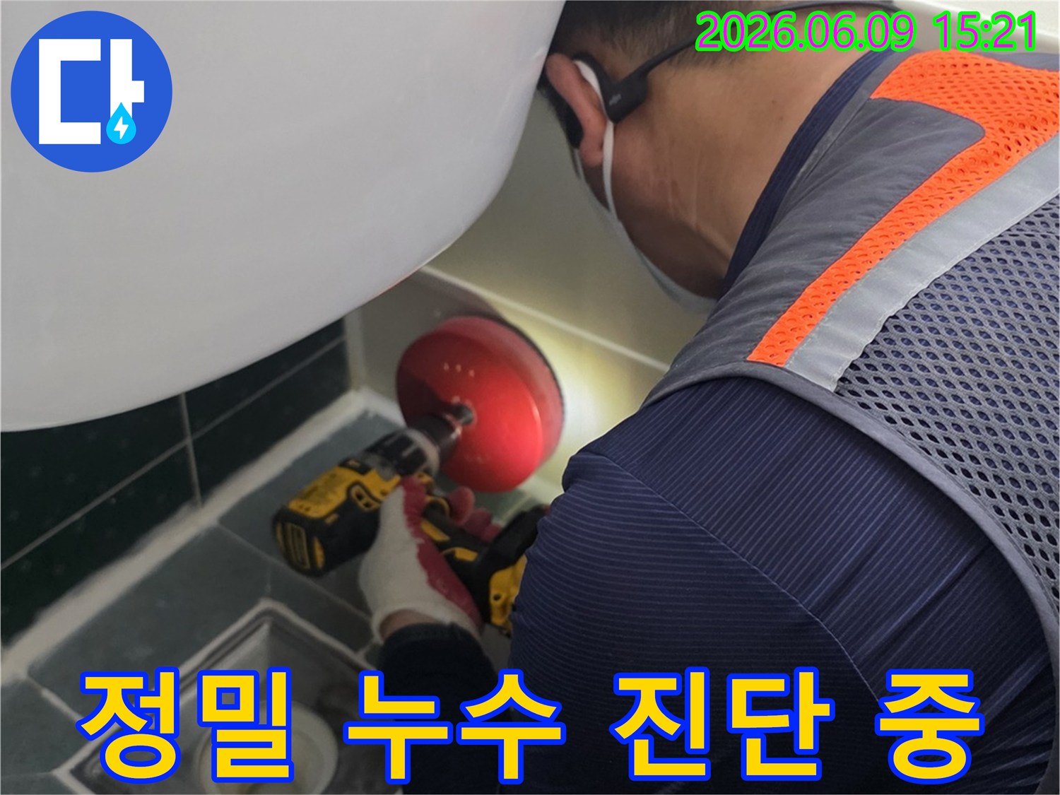 안전-조끼를-입은-엔지니어가-전동-드릴을-사용하여-욕실-배수구-주변을-점검하는-모습