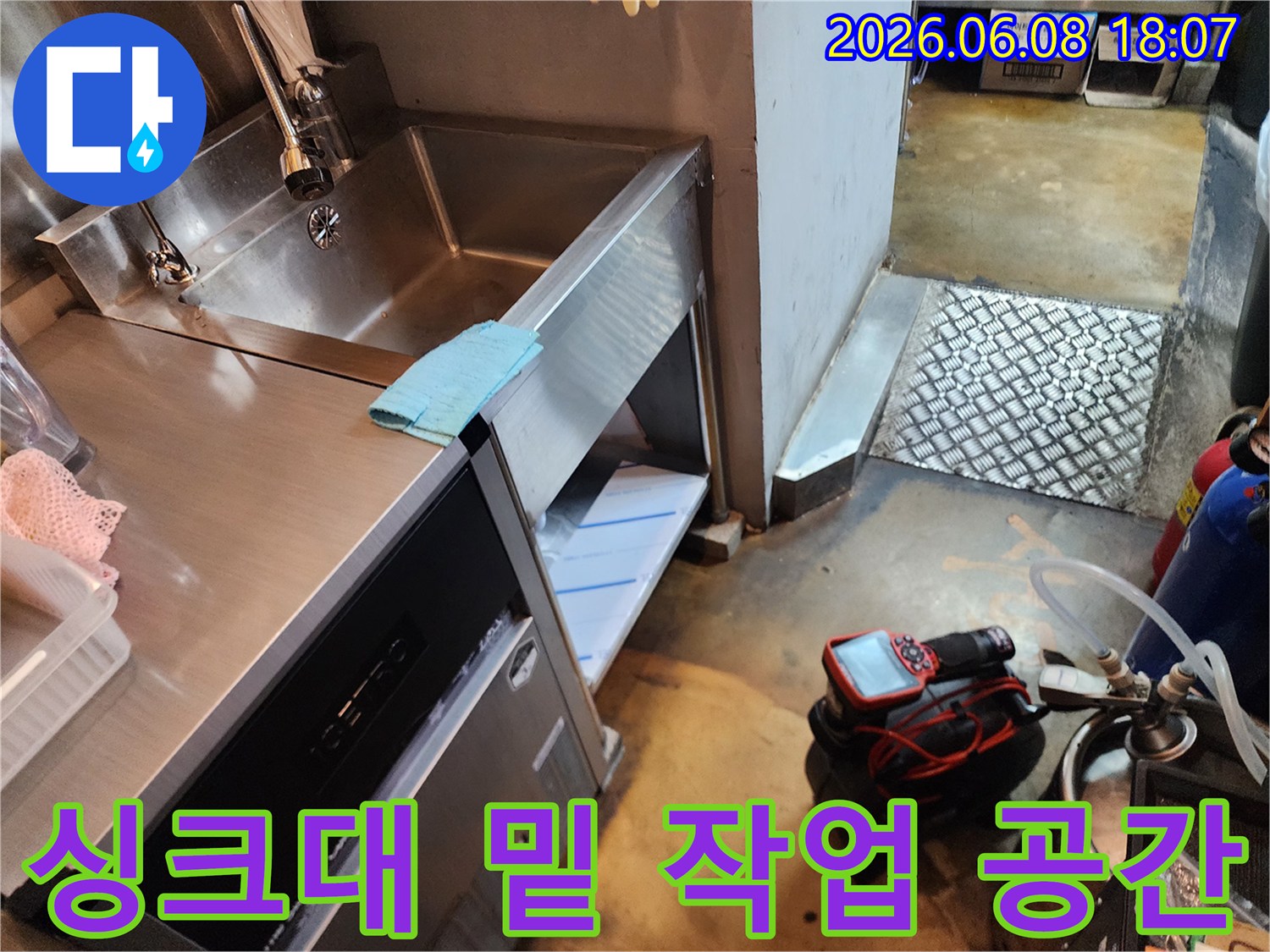 스테인리스 싱크대 아래 좁은 공간에 놓인 배관 점검용 석션 장비