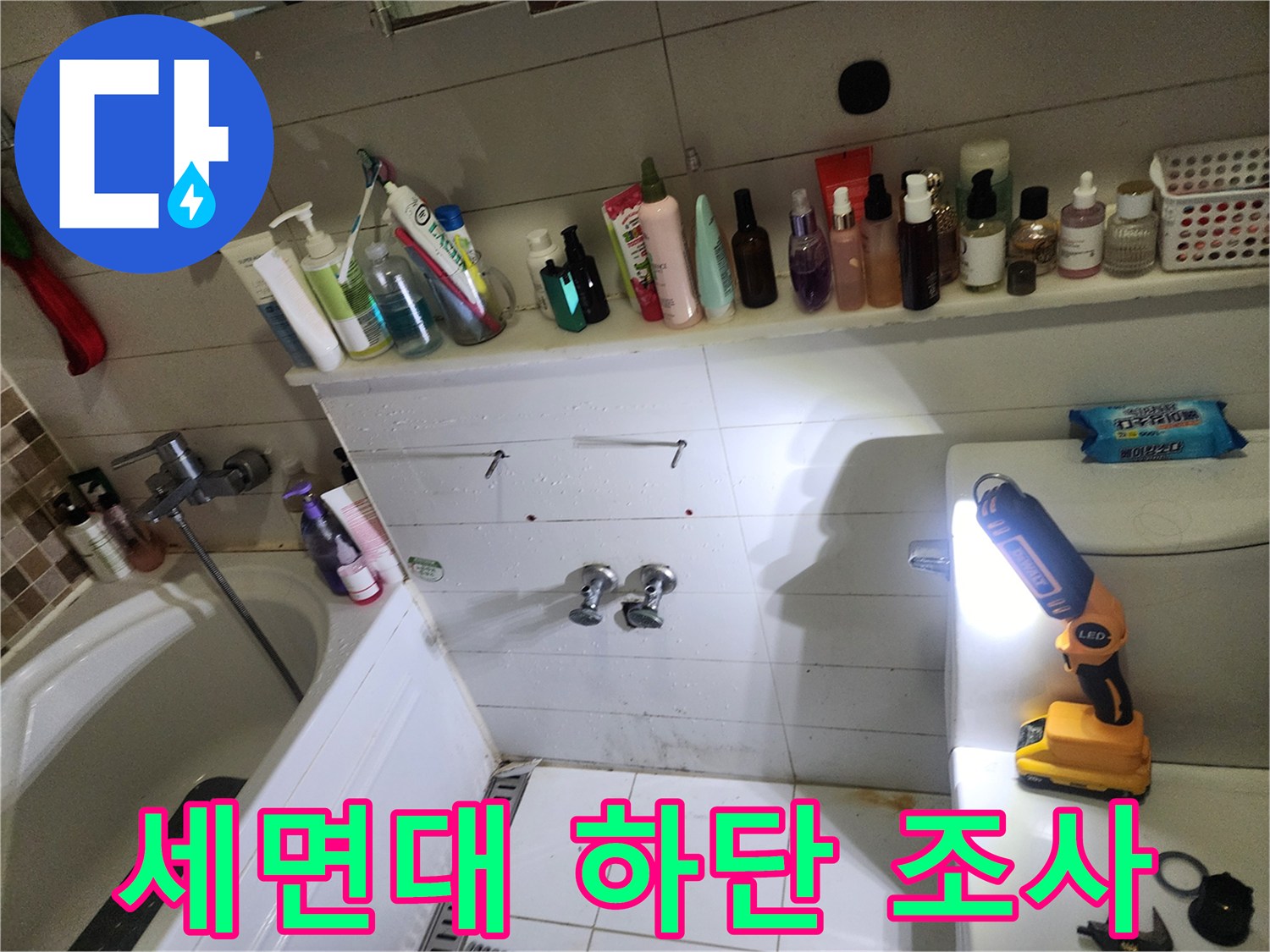 조명을 사용하여 세면대 벽면 타일 틈새의 습기 상태를 점검하는 장면
