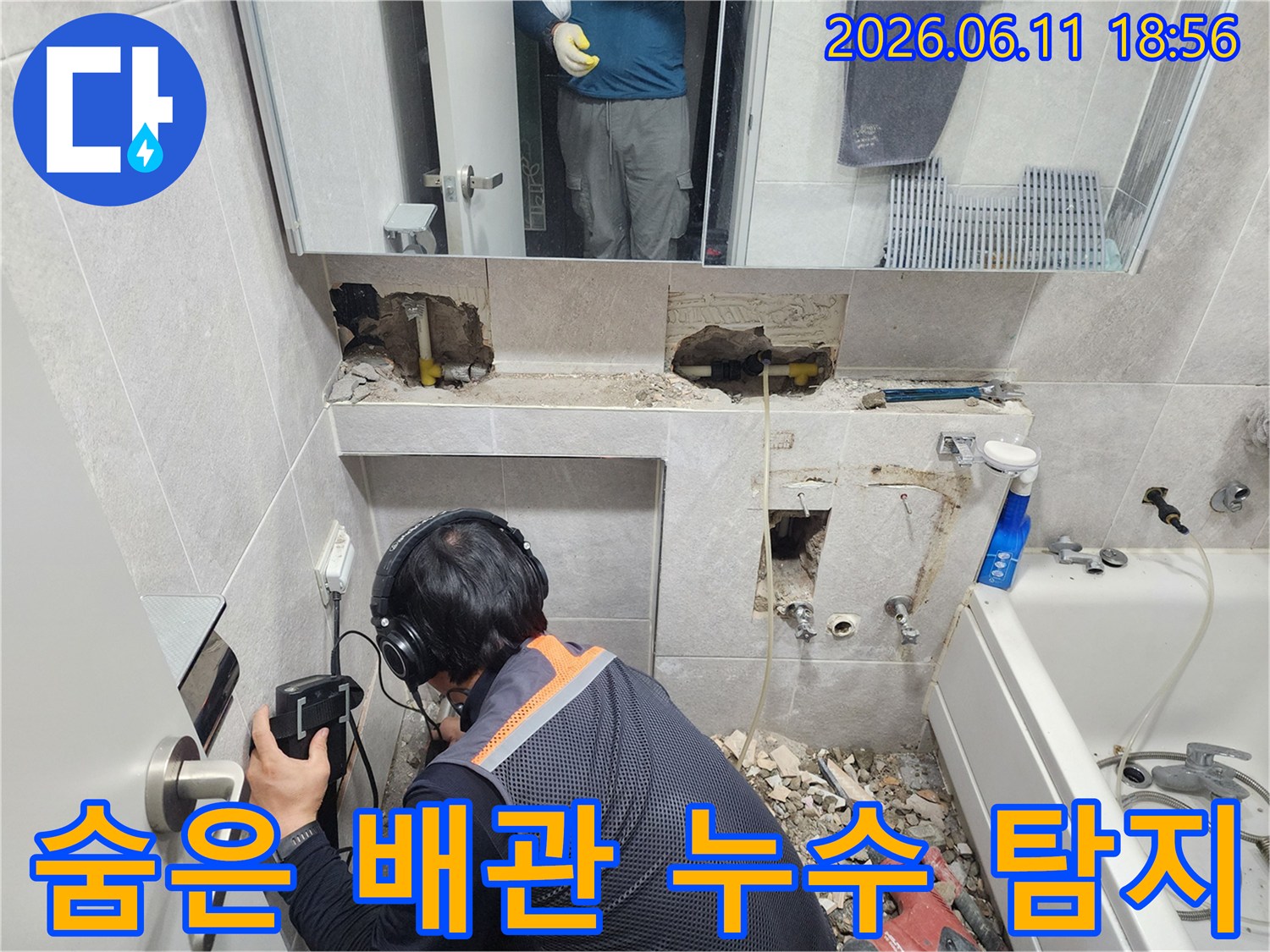 전문가가-누수 탐지 장비를 사용하여-욕실 벽면의-미세한 누수음을 듣고 있는 현장