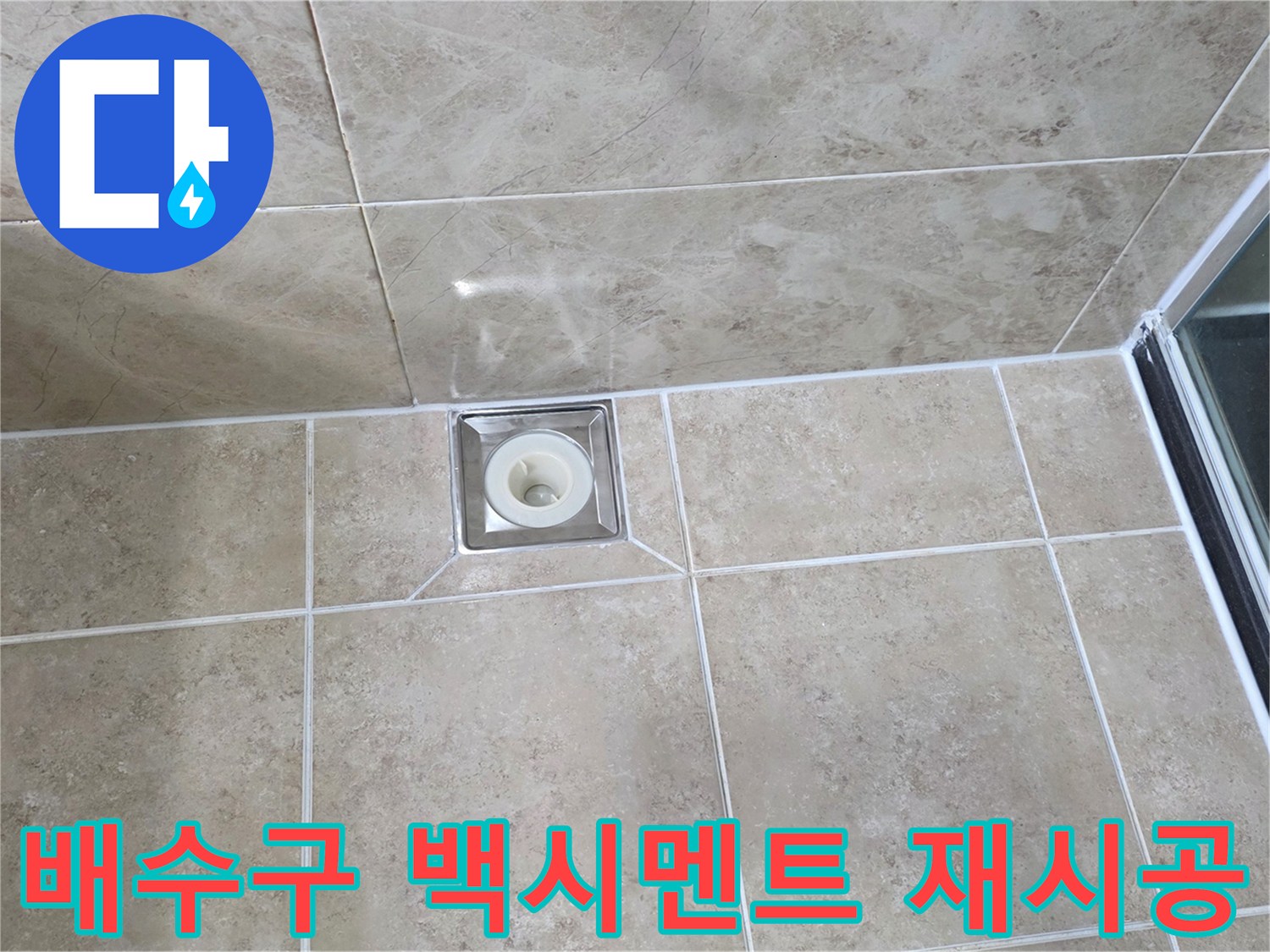 베이지색 타일 바닥에 설치된-사각형 금속 배수구의 모습으로-주변 백시멘트의 마감 상태를 보여줍니다