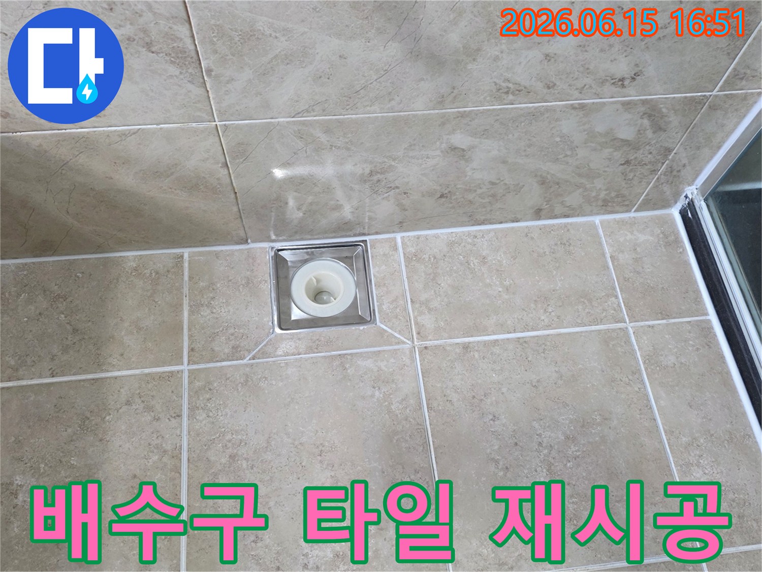베이지색 타일 바닥에 위치한-사각형 금속 배수구의 모습으로-주변 타일의 접합부와-줄눈의 상태를 상세히 보여줍니다