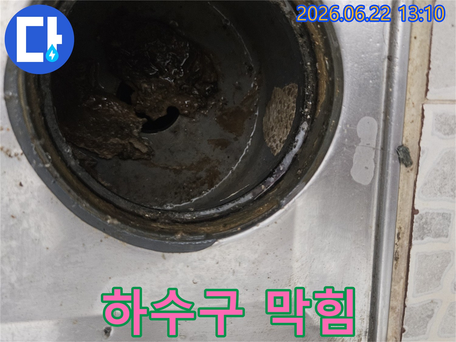 오래된 배수구에 쌓인 이물질과-슬러지를 담은 사진으로-배관 막힘으로 인한 누수 가능성을 시사합니다.