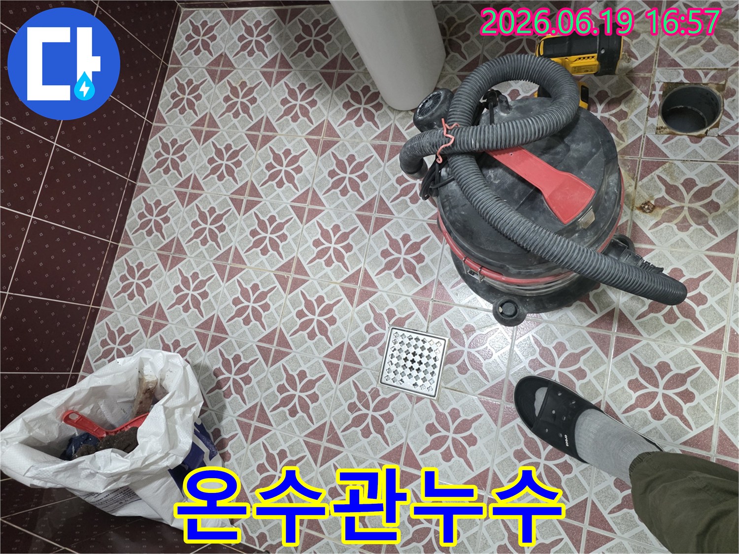 물기 제거를 위해 사용된-산업용 습식 청소기가-욕실 바닥에 놓여 있고-배수구와-작업자의 발이 함께 보이는 장면