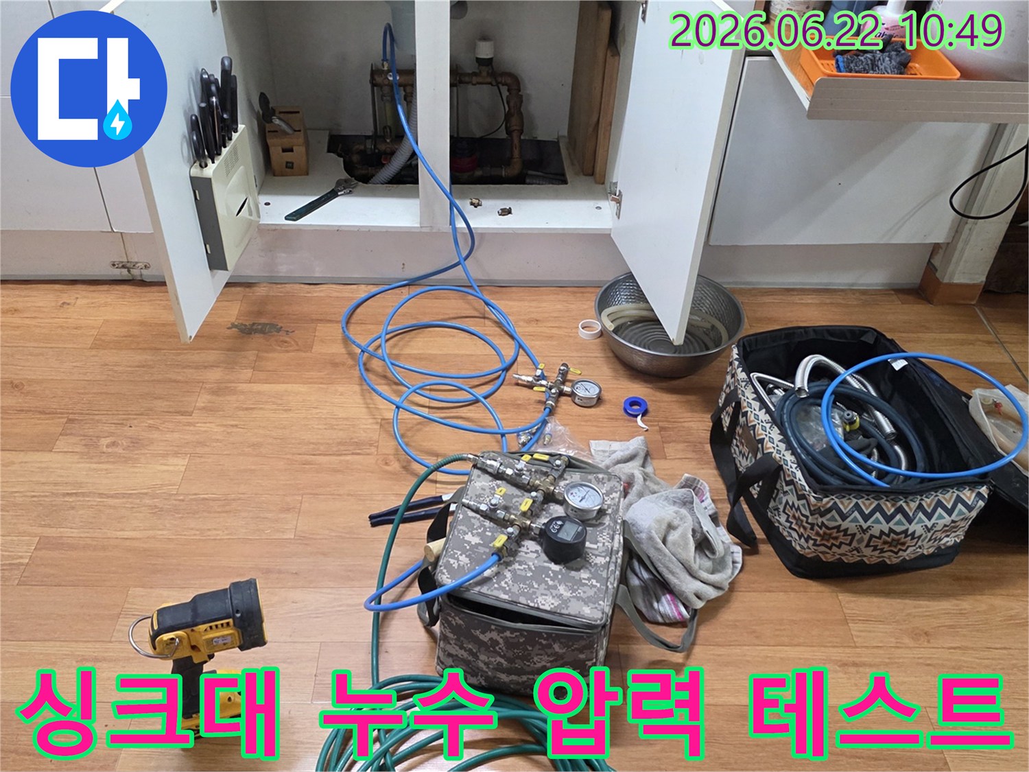 싱크대 하부 배관의 누수 여부를 확인하기 위해 압력 테스트 장비를 연결하고 있는 전문 기술자의 모습-입니다.