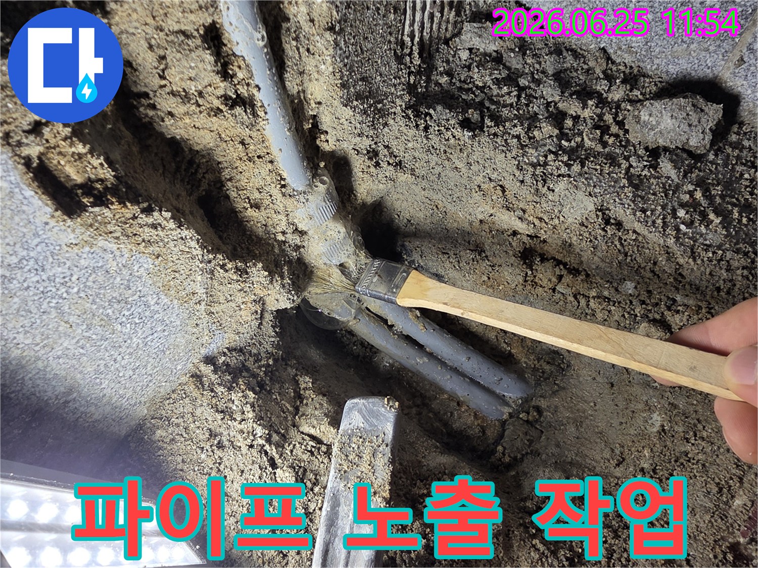 숙련된 기술자가 파묻힌 배관을 드러내기 위해 흙을 털어내는-정밀 누수 탐지 작업 현장입니다