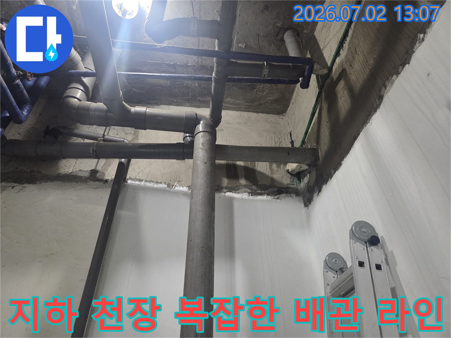 지하 공간의 천장과 벽면에 설치된 복잡한 회색 배관망-누수 진단을 위해 확인 중인 모습