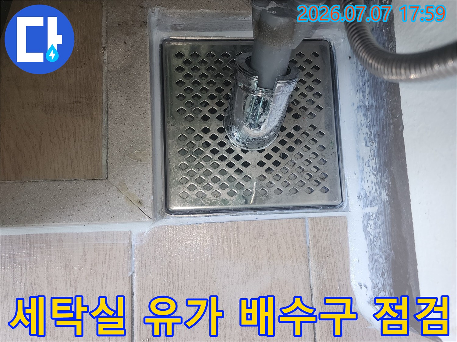 세탁실 바닥에 설치된 금속 재질의 배수구와 연결된 세탁기 호스