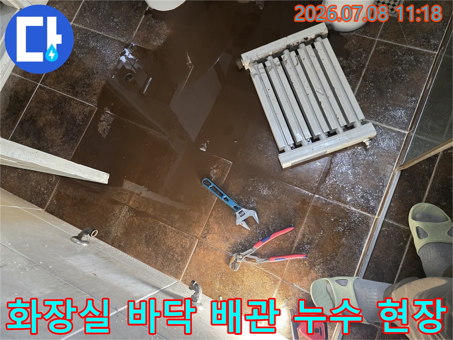 화장실 바닥에 물이 고여 있고 수리용 공구와 철거된 라지에터가 놓인 장면