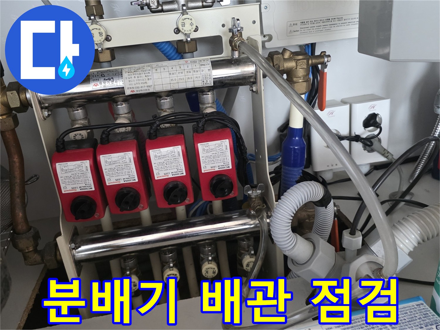 보일러 분배기에 연결된 여러 개의 붉은색 유량 조절 밸브와 배관 상태를 정밀하게 점검하는 모습입니다.