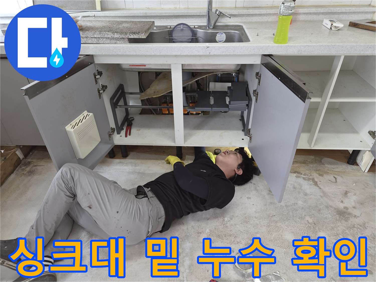 싱크대 아래 공간에서 배관의 물샘 흔적을 조사하는 작업자