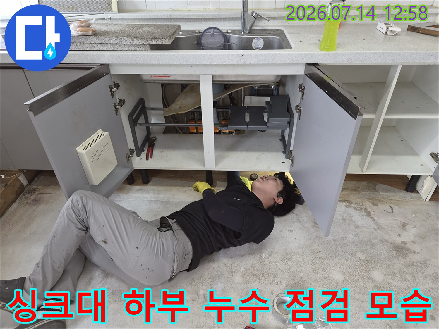작업자가 싱크대 아래 좁은 공간에 누워 배관 상태를 확인하고 있는 모습