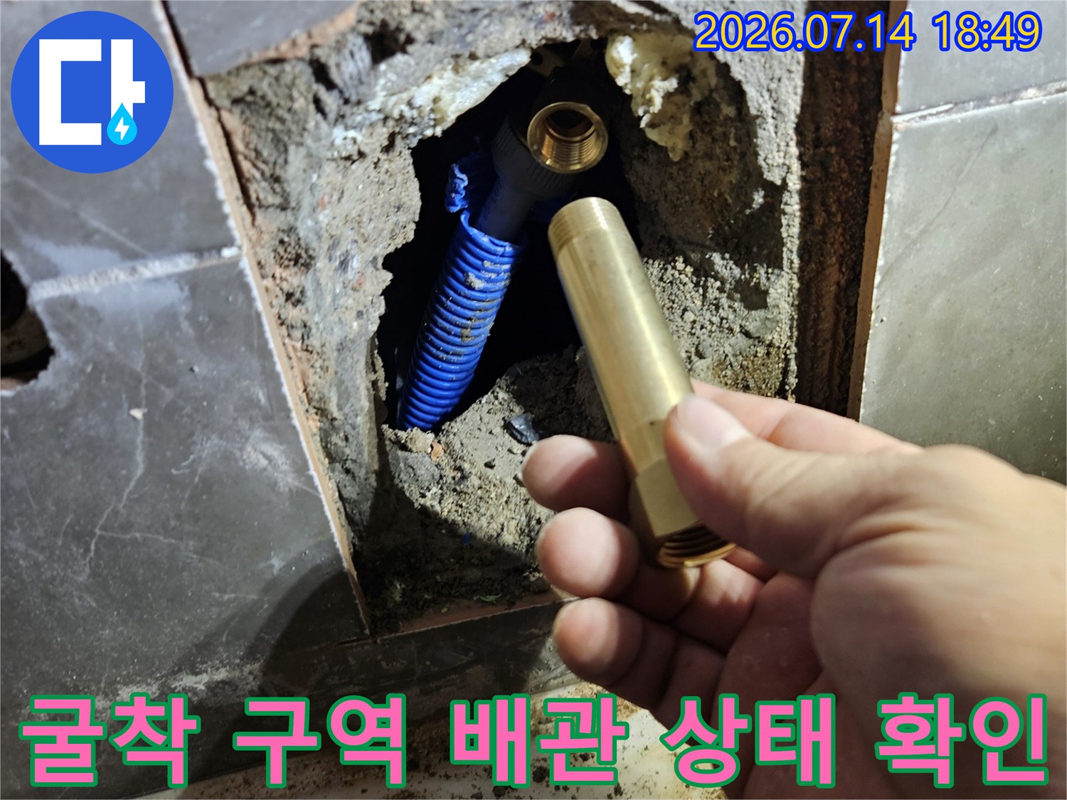 타일이 제거된 공간 속에서 파란색으로 감싸진 배관과 황동 수전 부품을 점검하는 장면