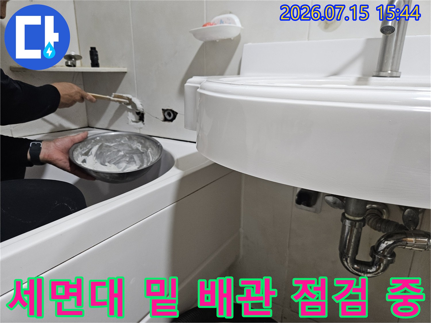 세면대 하단에 위치한 노후된 수도 배관을 전문 장비와 수작업으로 확인하는 모습