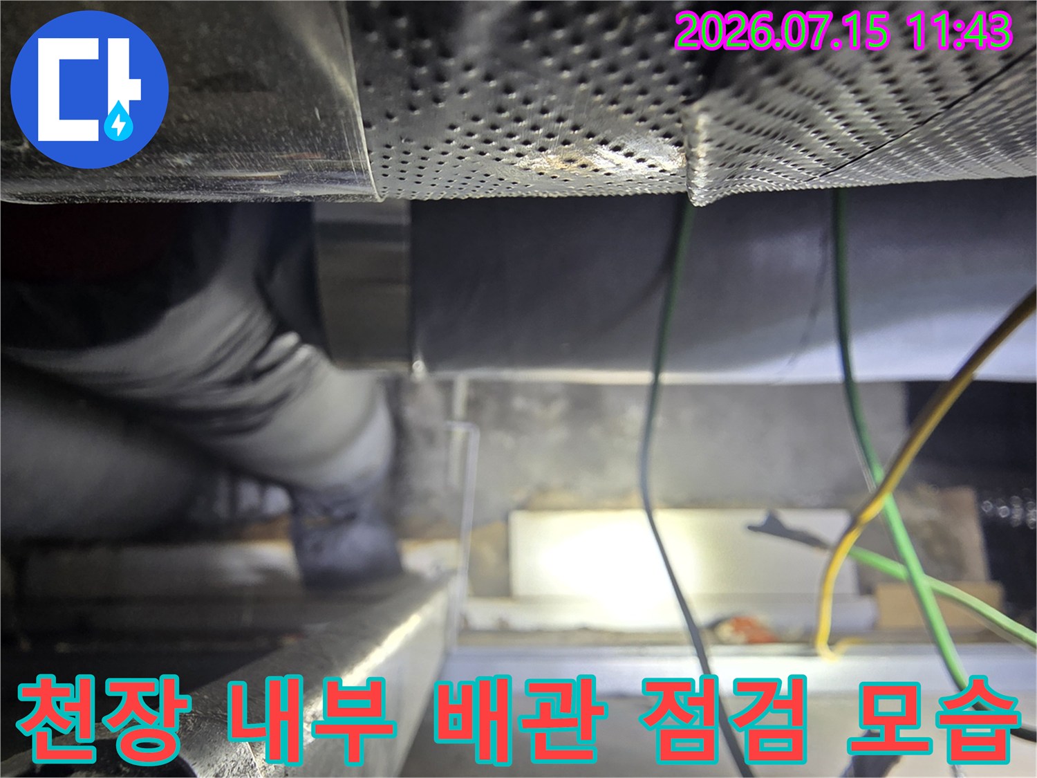 어두운 천장 내부 공간에서-보온재로 감싸진 배관과-전기선들을 확인하는-엔지니어의 작업 모습