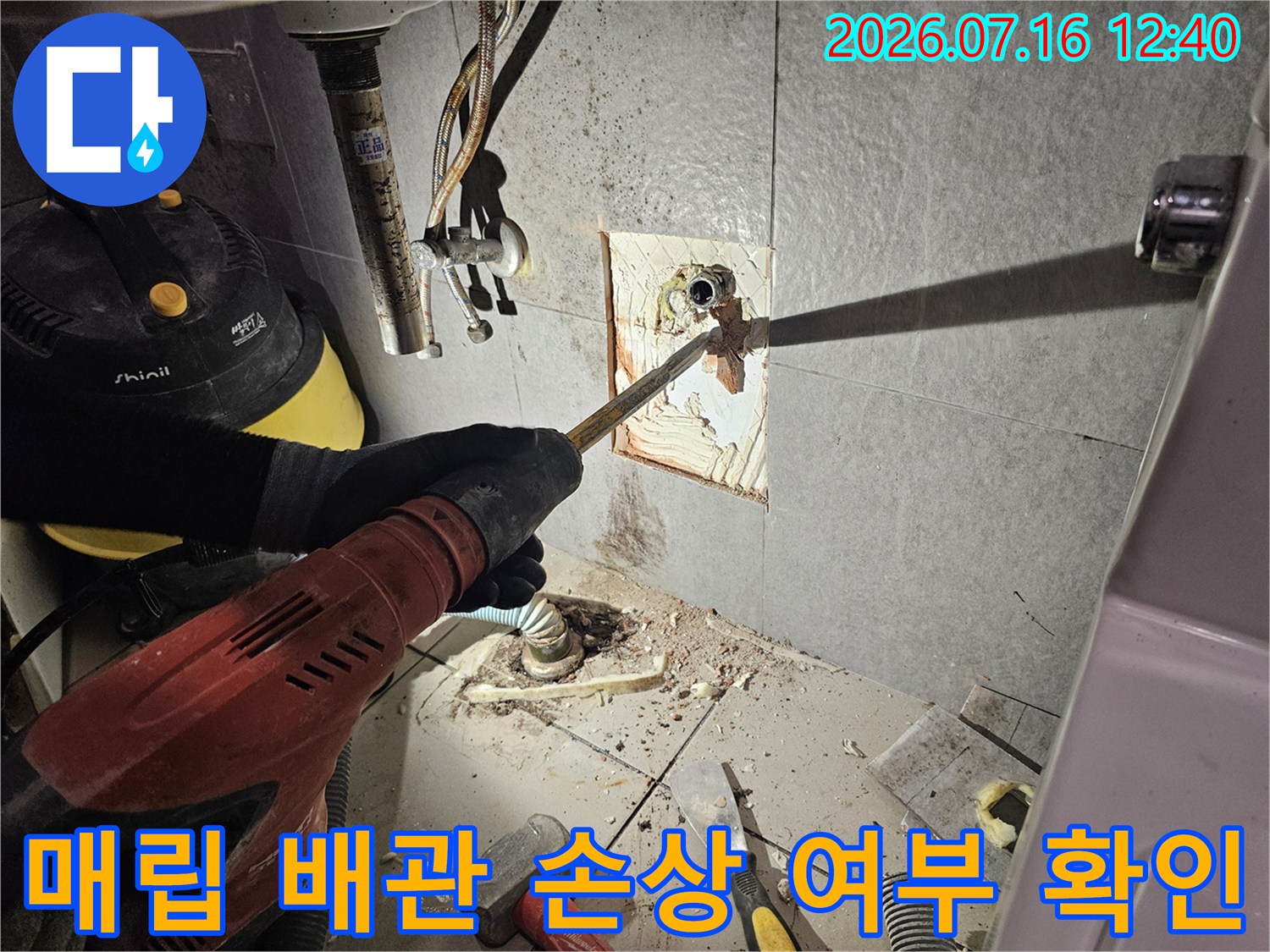 벽면을 파내어 드러난 매립형 수도 배관의 연결 상태를 꼼꼼히 점검하고 있는 공사 장면입니다.