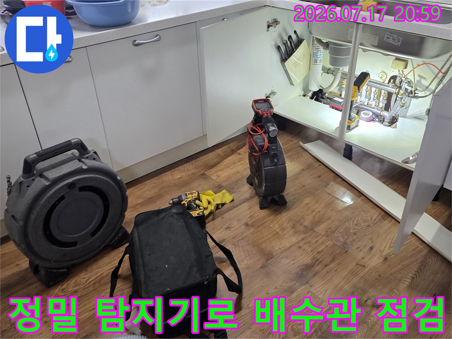 장비를 활용하여 싱크대 하단에 위치한 배수 라인의 이상 여부를 꼼꼼히 조사하는 모습
