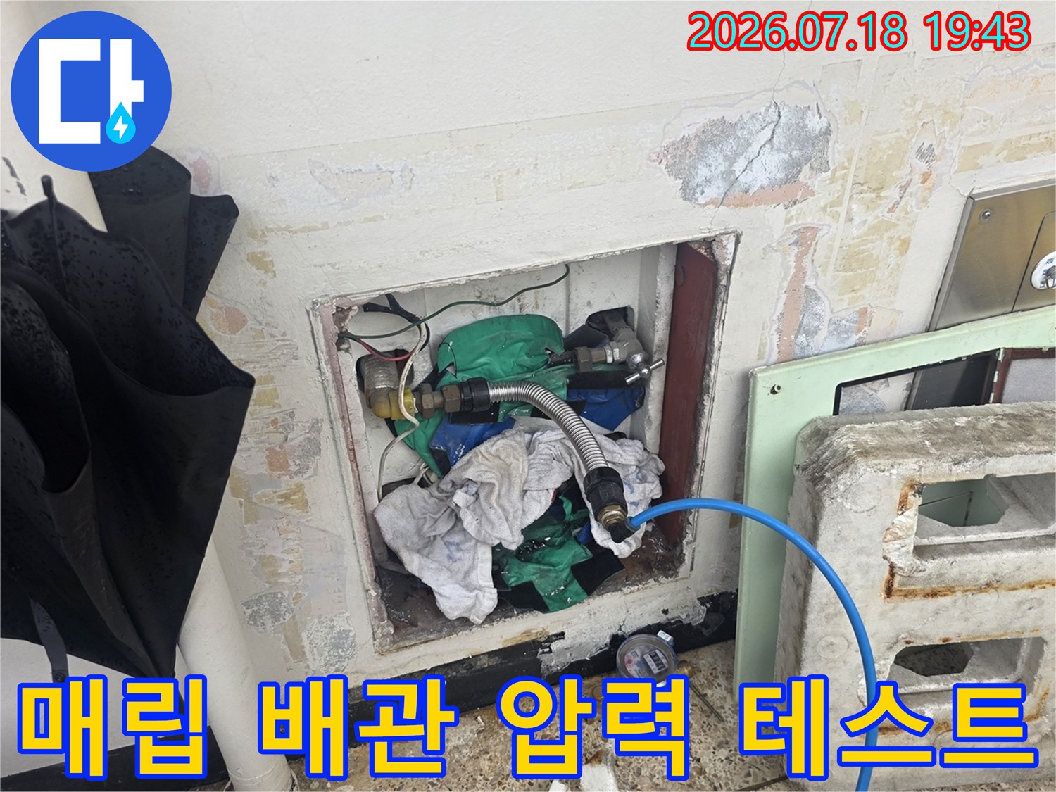 노출된 녹색 수도 배관에 파란색 호스를 연결하여 정밀 점검을 수행하는 장면