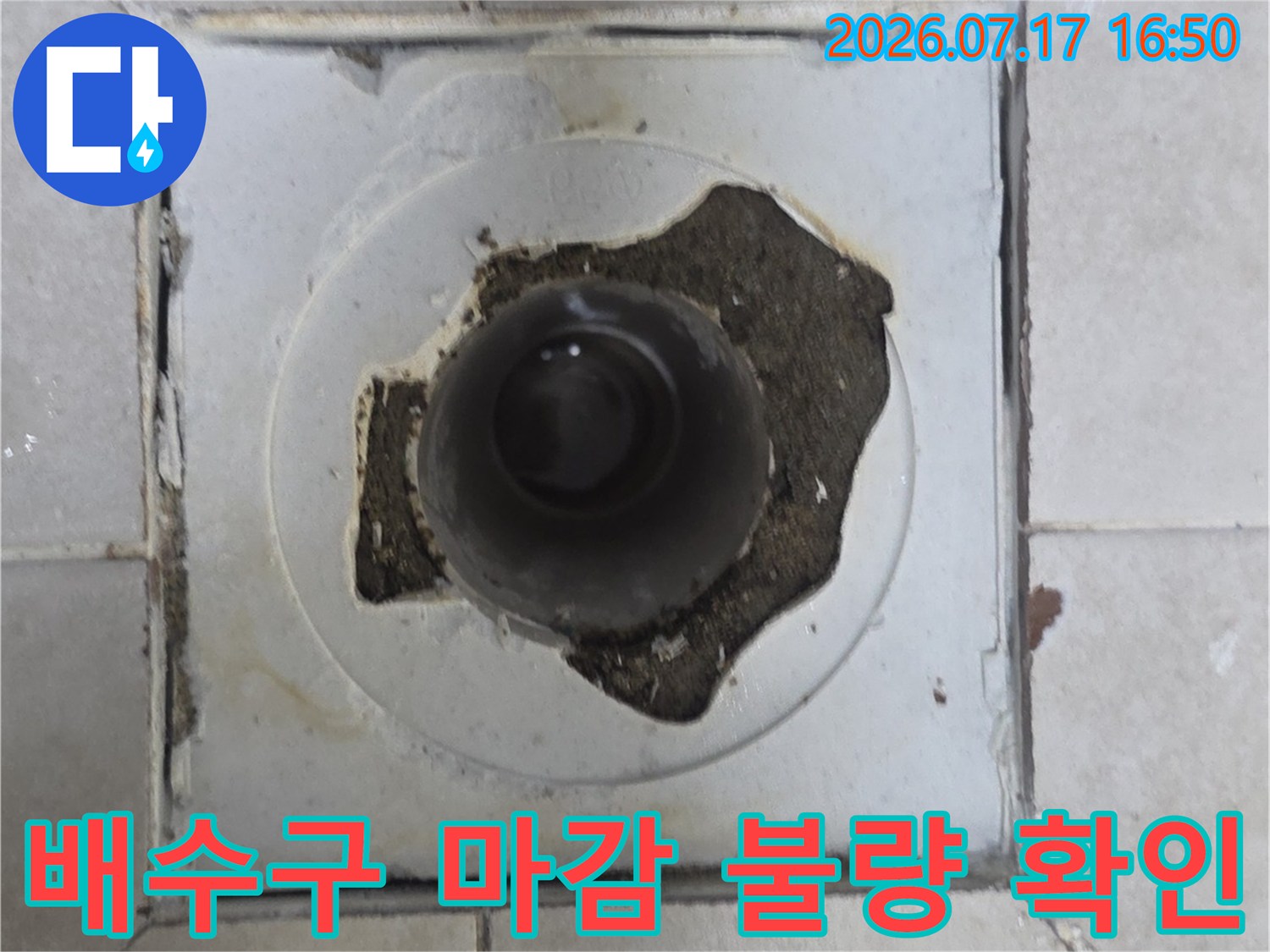 파손된 배수구 주변의 노출된 파이프와 훼손된 타일 마감재