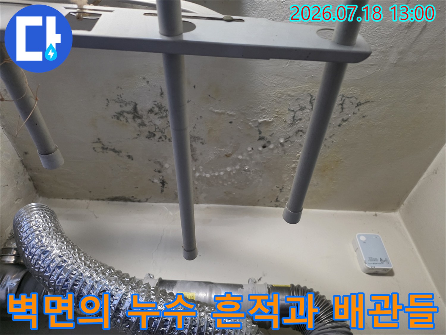 배관 지지대와 파이프 주변으로 넓게 퍼진 습기 얼룩과 변색된 벽면의 모습