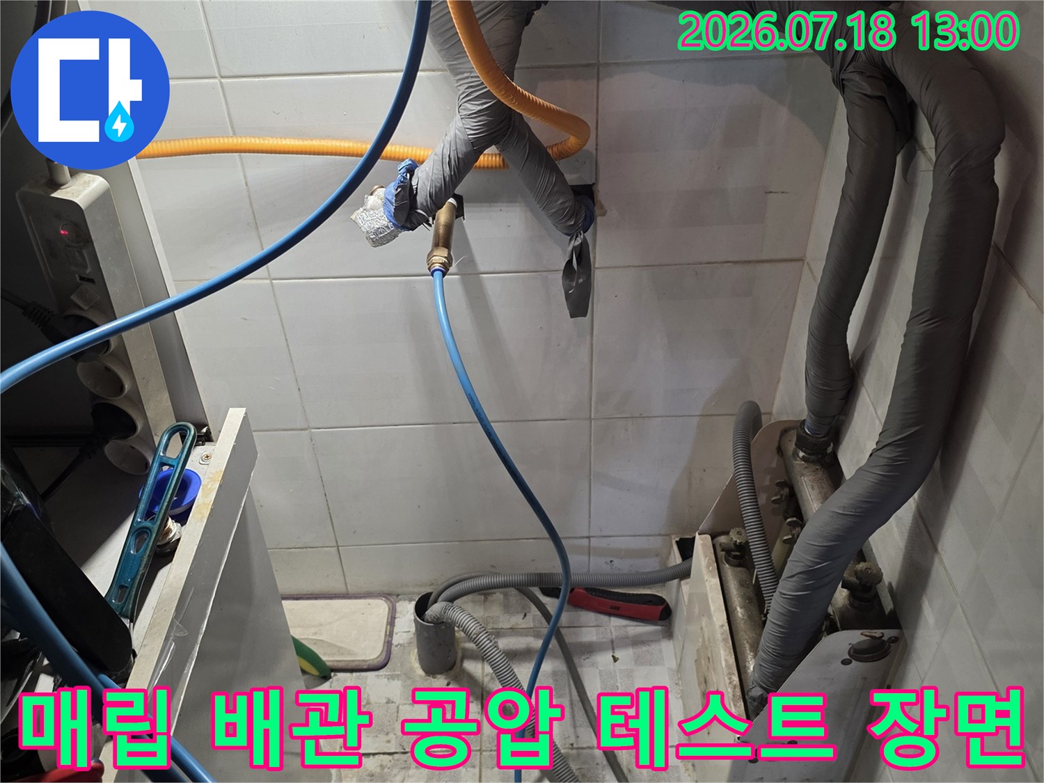 흰색 타일 벽면의 회색 보온재 처리된 배관들과 파란색 탐지 장비 호스가 연결된 모습-누수 검사 중