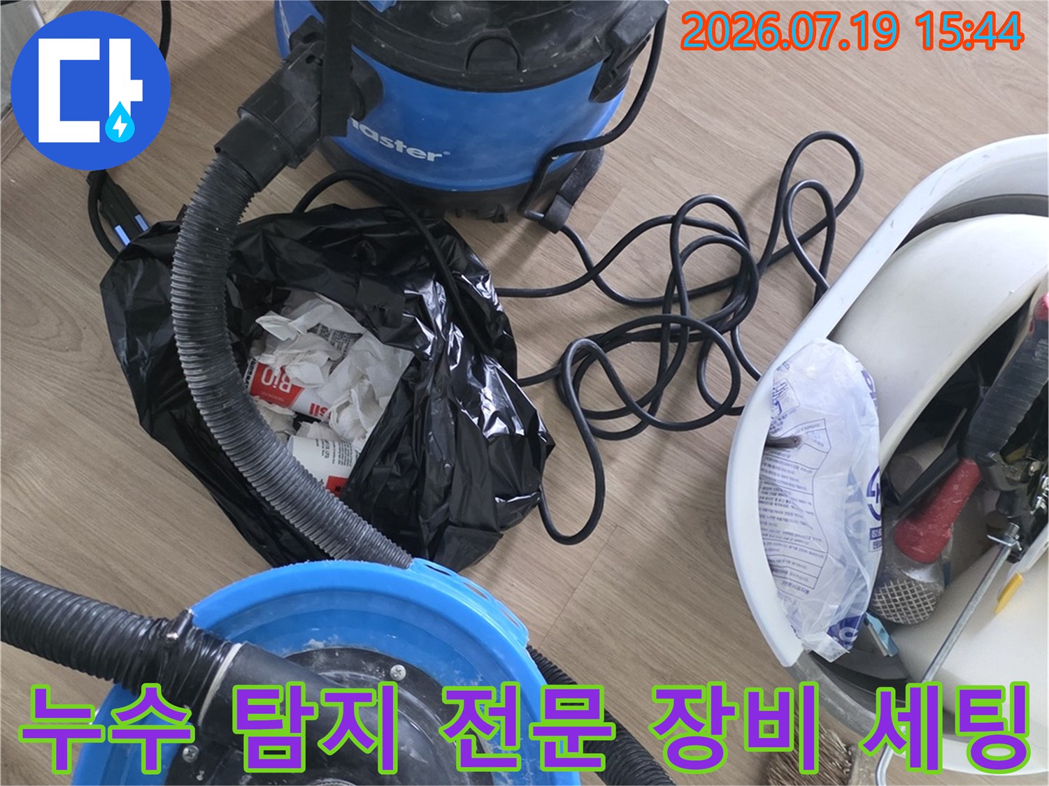 바닥에 놓인 파란색 습식 청소기와 각종 누수 점검 공구가 담긴 바구니-현장 작업 준비 모습