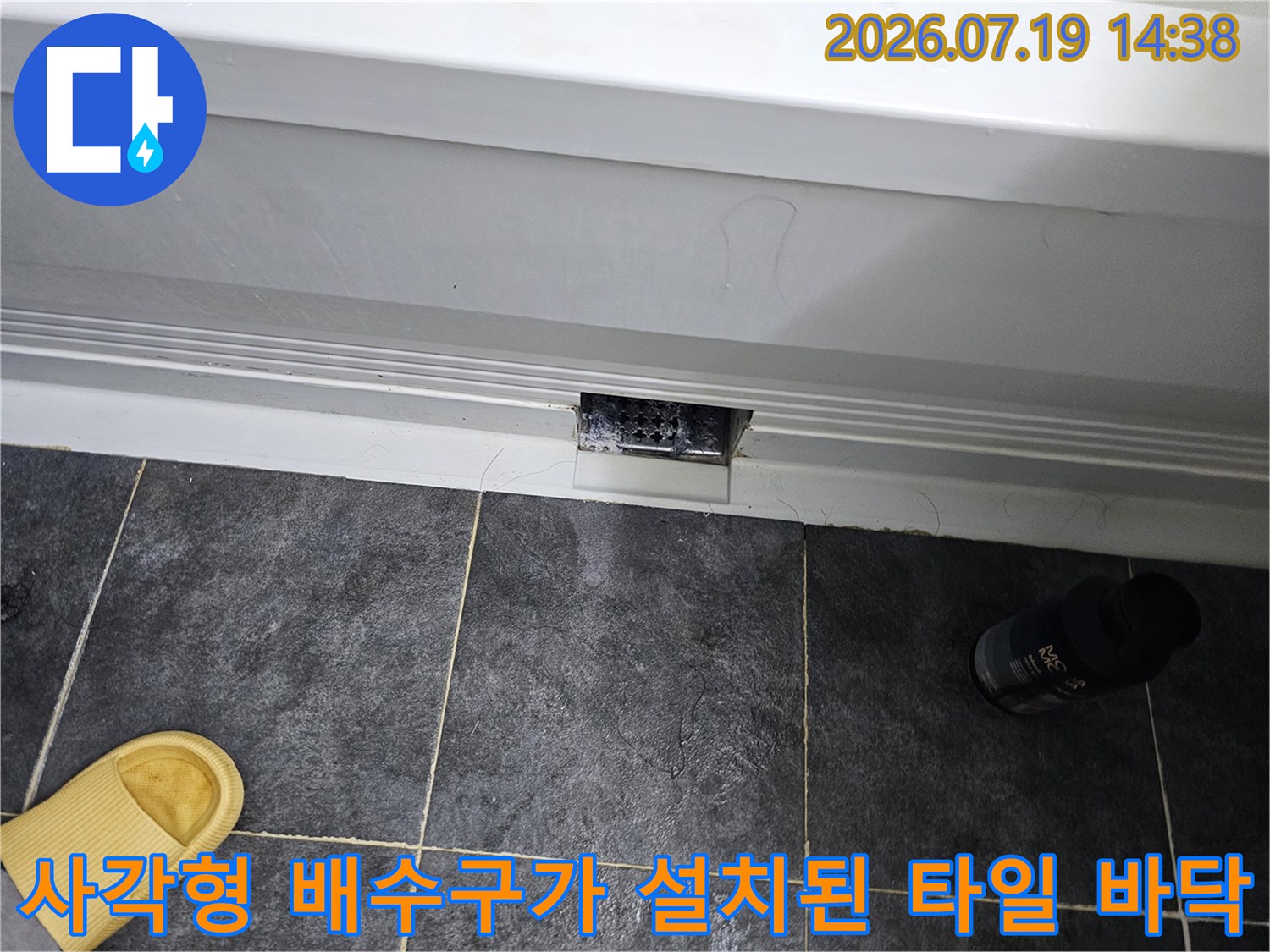 어두운 색상의 욕실 타일에-매립된 직사각형 모양의 하수구 입구 사진