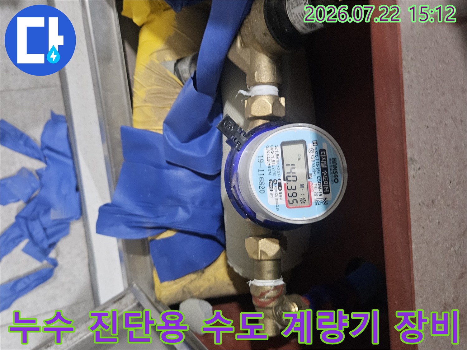 금속 배관 사이에 설치된 숫자판이 보이는 계량기와 주변의 파란색 보양재-작업 현장 사진