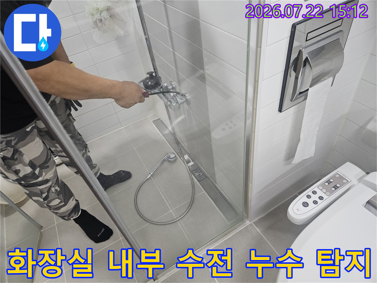 작업자가 샤워 시설의 수도 밸브 부근을 세밀하게 살펴보고 있는 욕실 내부 전경