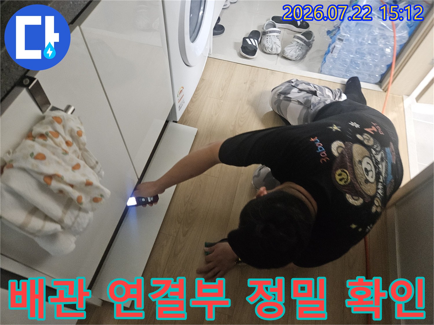 작업자가 세탁실 싱크대 아래쪽 좁은 공간으로 손전등을 비추며 배관을 살피는 모습
