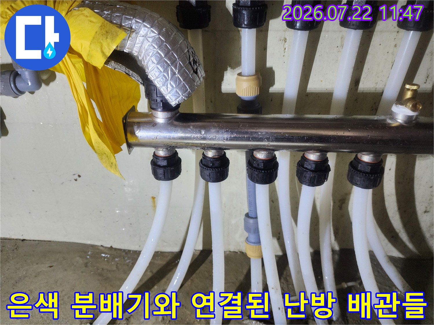 보일러 시스템의 핵심인 금속 분배기에 여러 갈래의 흰색 PEX 배관이 연결되어 있는 전경