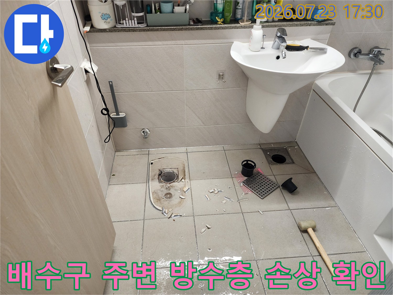 욕실 바닥 타일 사이에 설치된 배수구 유가가 제거되어 내부가 노출된 장면