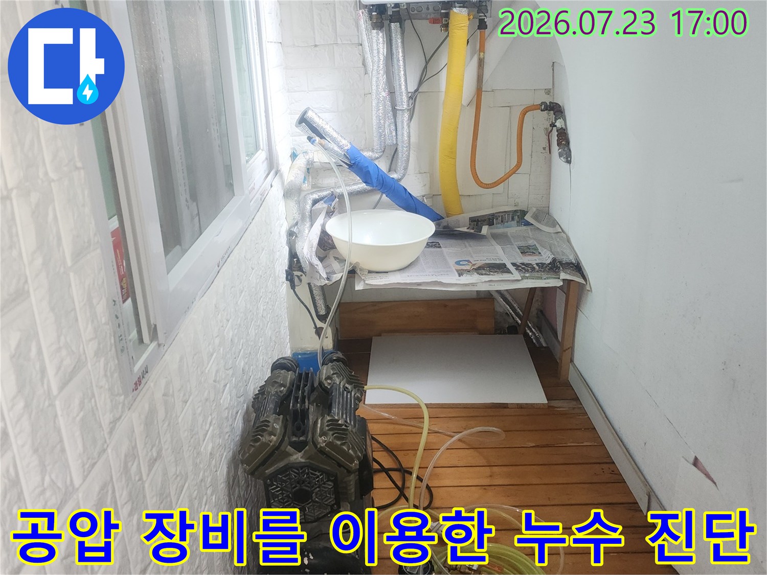 흰색 벽지와 나무 판넬 배경에 배치된 누수 탐지용 컴프레셔와 호스