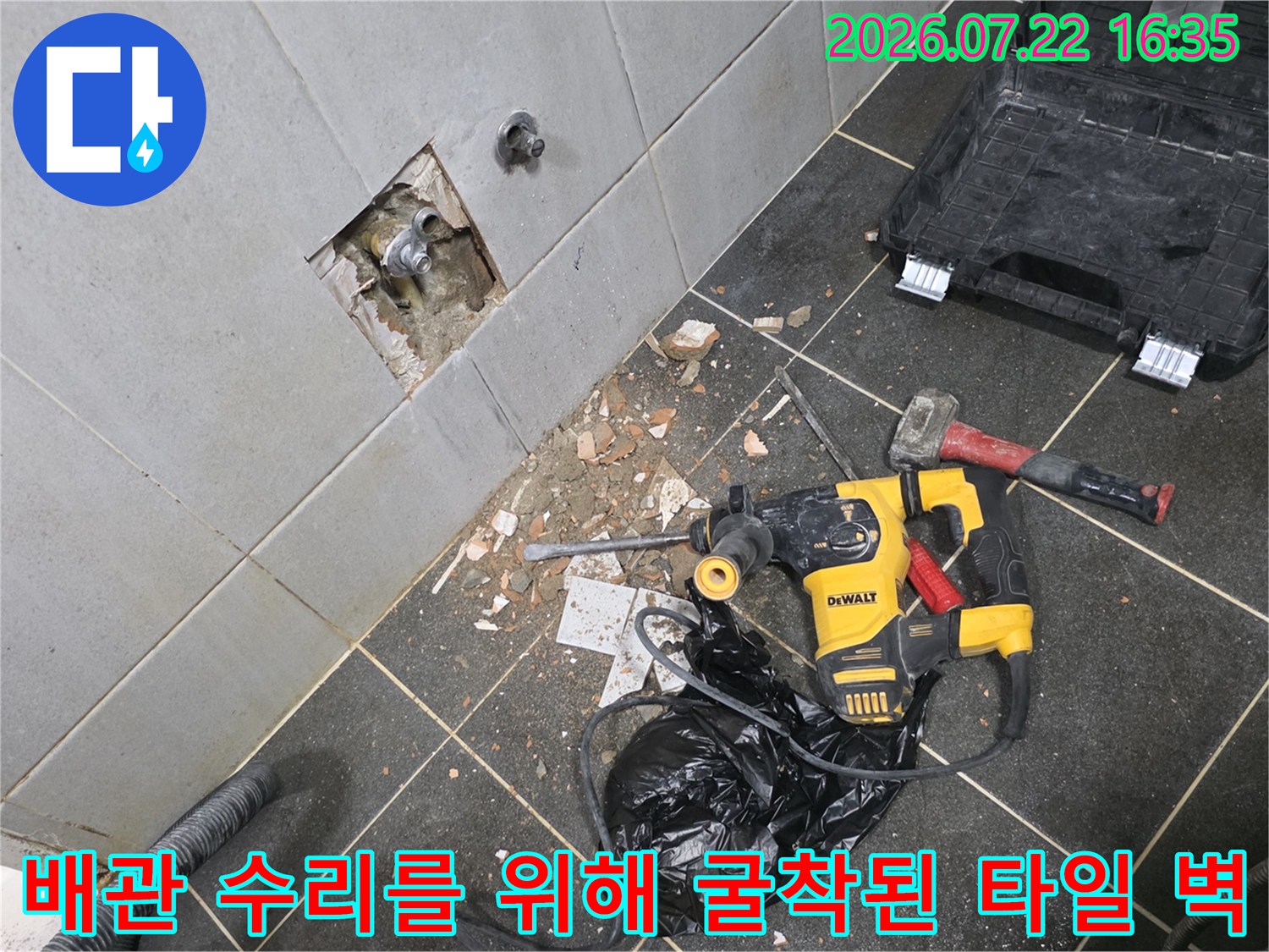 벽면의 사각 구멍을 통해 내부 배관이 드러나 있으며-바닥에 노란색 전동 드릴과 검은색 케이스가 놓여 있음