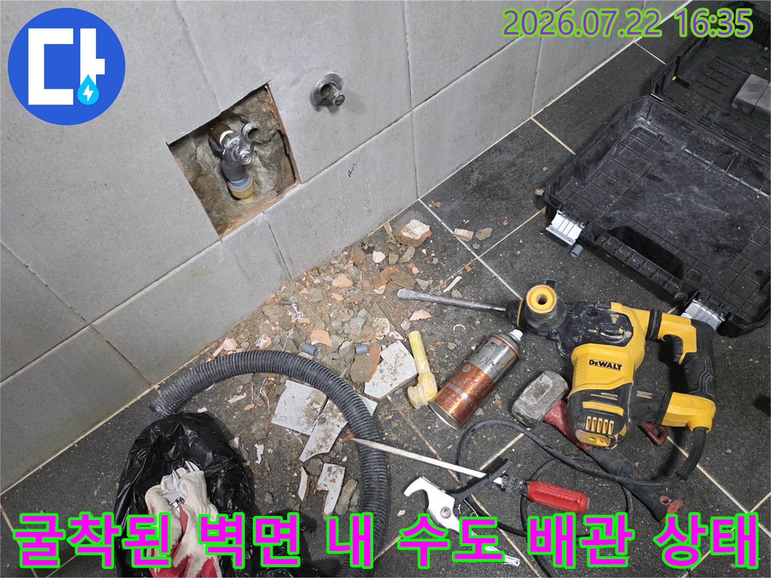 타일이 제거된 사각형 구멍 속으로 은색과 회색의 수도 배관 연결 부위가 보이는 사진